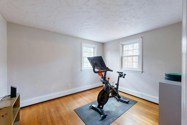 exercise area featuring a textured ceiling, wood finished floors, baseboards, and a baseboard radiator