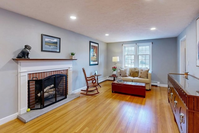 living area featuring light wood-style floors, baseboards, baseboard heating, and a fireplace