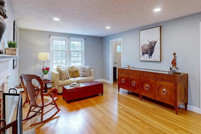 sitting room featuring light wood finished floors, a fireplace, a textured ceiling, and baseboards