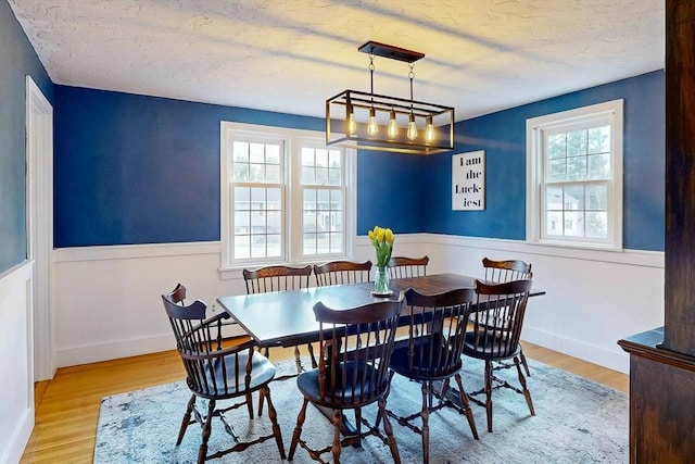 dining space with a wainscoted wall, a textured ceiling, and wood finished floors