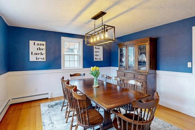 dining space featuring a wainscoted wall, wood finished floors, and a baseboard heating unit