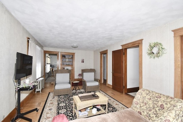 living area with radiator, light wood finished floors, baseboards, and a textured ceiling