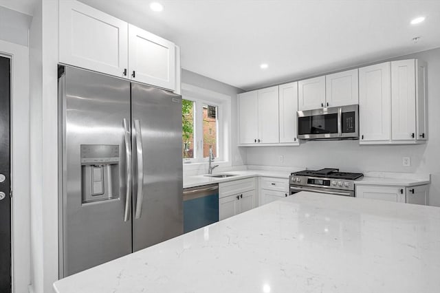 kitchen with stainless steel appliances, a sink, light stone countertops, white cabinetry, and recessed lighting