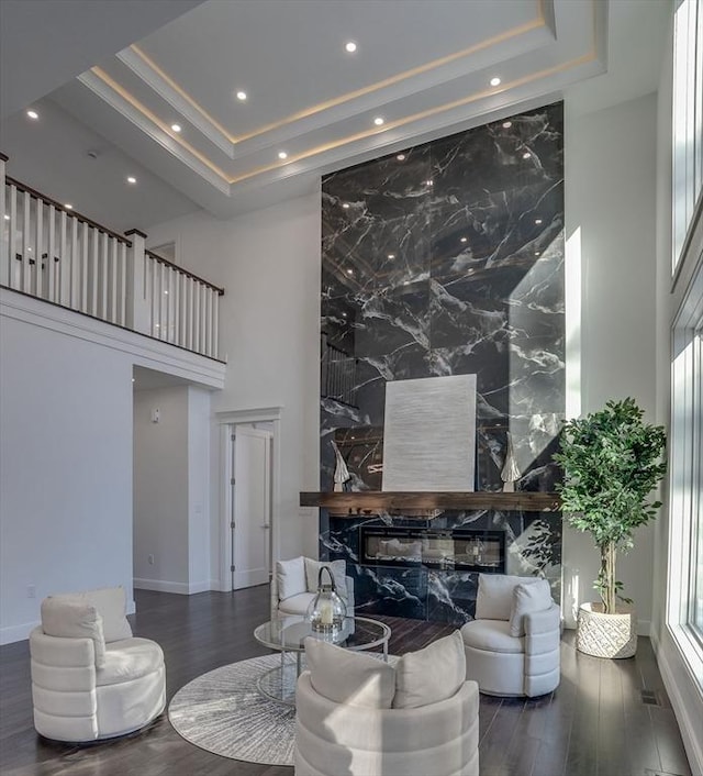 living room with dark wood-type flooring, a premium fireplace, a raised ceiling, and a high ceiling