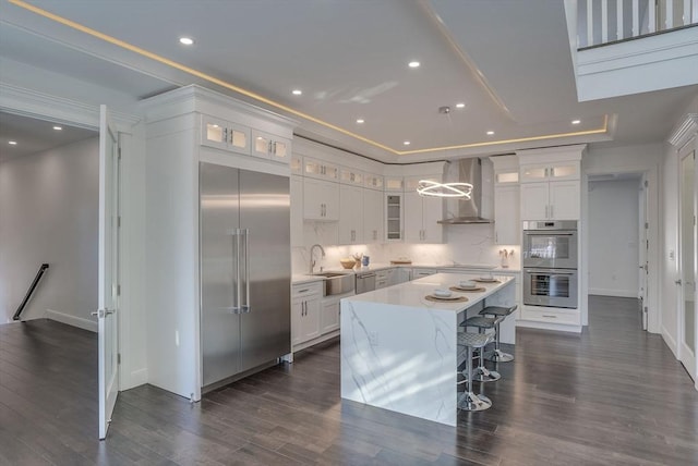 kitchen featuring wall chimney exhaust hood, stainless steel appliances, a kitchen island, and white cabinets