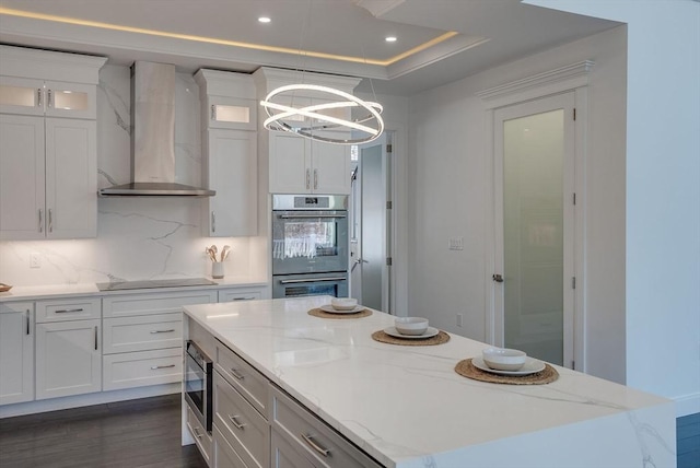 kitchen featuring stainless steel appliances, white cabinetry, a kitchen island, and wall chimney range hood