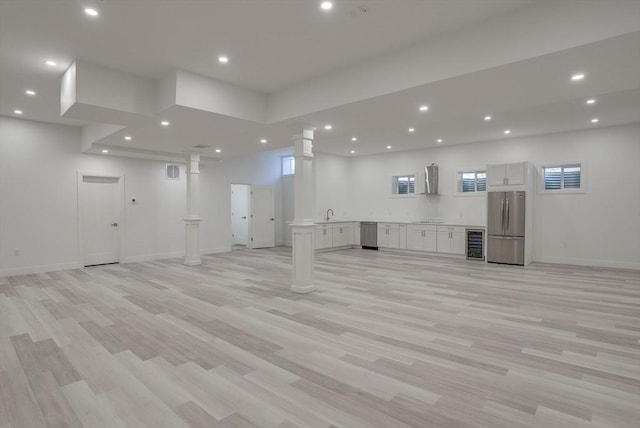 basement with a wealth of natural light, light hardwood / wood-style flooring, beverage cooler, and stainless steel refrigerator