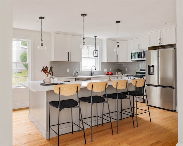 kitchen featuring light wood-type flooring, stainless steel appliances, plenty of natural light, and white cabinetry