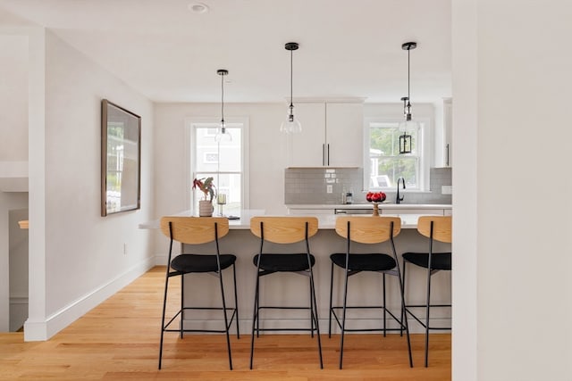 kitchen with light hardwood / wood-style flooring, white cabinetry, hanging light fixtures, and a breakfast bar area