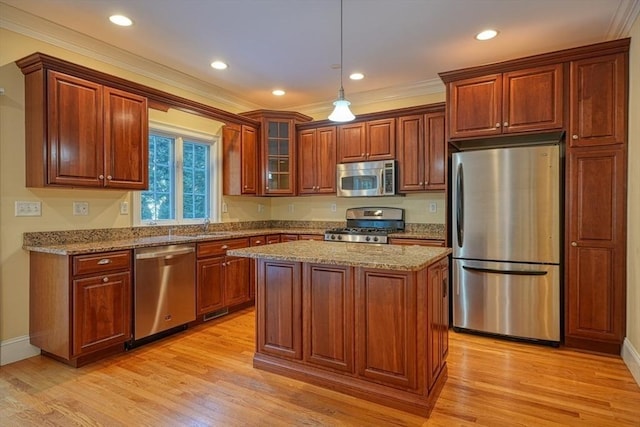 kitchen with light wood-type flooring, appliances with stainless steel finishes, a kitchen island, pendant lighting, and light stone countertops