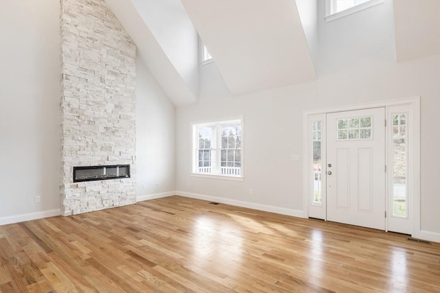 unfurnished living room with light wood-type flooring, a fireplace, and a high ceiling