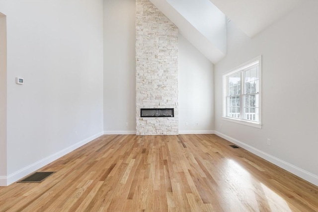 unfurnished living room with light wood-type flooring, high vaulted ceiling, and a stone fireplace