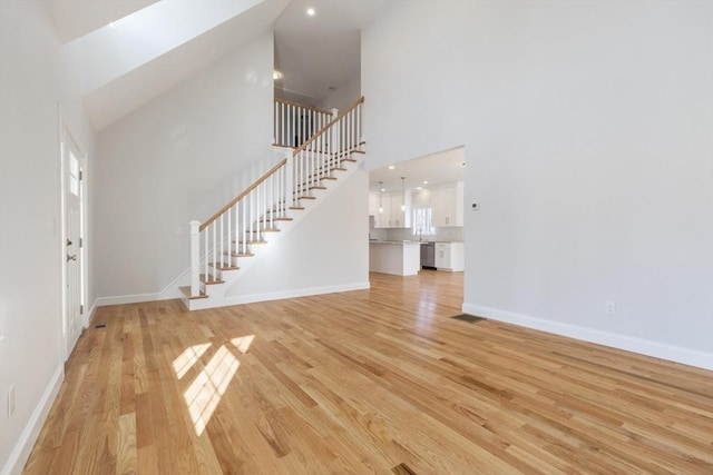 unfurnished living room featuring a skylight, light hardwood / wood-style flooring, and high vaulted ceiling