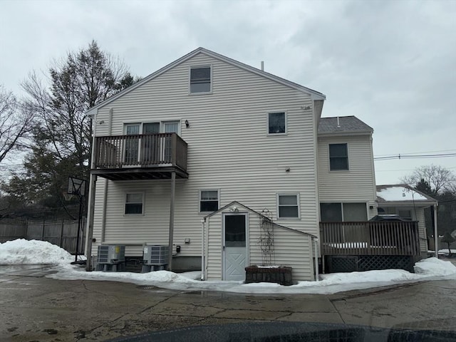 snow covered back of property with cooling unit and a balcony