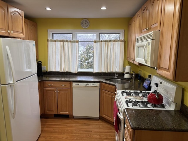 kitchen featuring white appliances, dark stone counters, brown cabinetry, light wood-style floors, and a sink