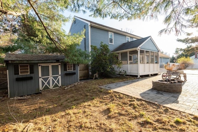 rear view of property with a storage shed, a sunroom, an outbuilding, a patio area, and a fire pit