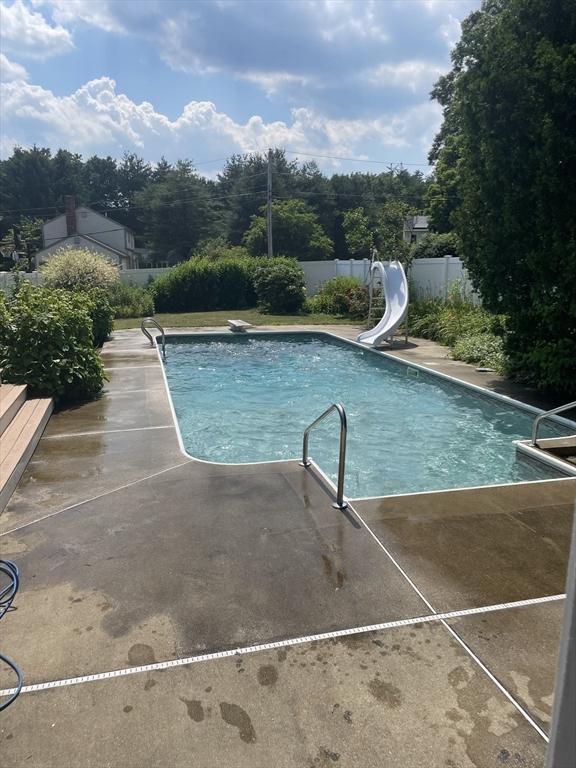 view of swimming pool featuring fence, a diving board, a water slide, a fenced in pool, and a patio