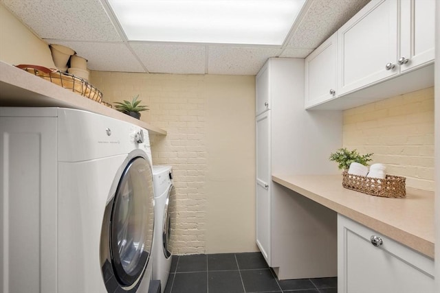 clothes washing area with brick wall, dark tile patterned flooring, washing machine and clothes dryer, and cabinet space