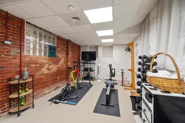 exercise room with a paneled ceiling, visible vents, and brick wall