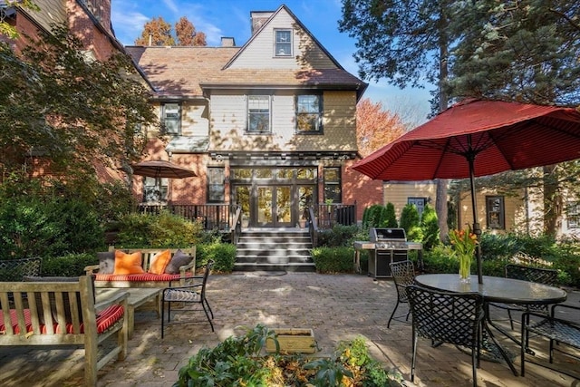 rear view of house with a deck, outdoor dining area, brick siding, a chimney, and a patio area