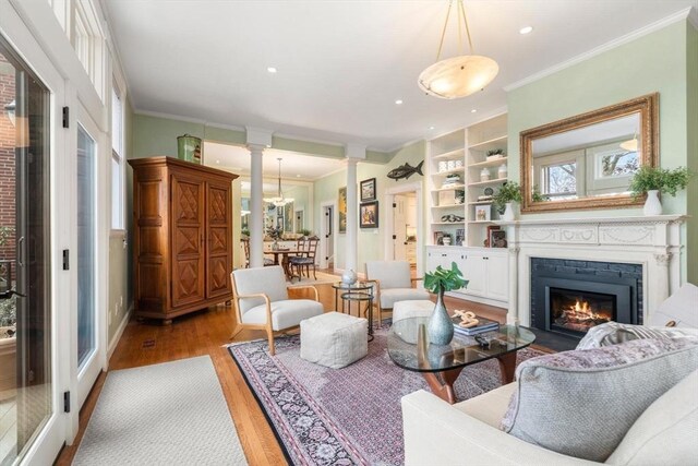 living room with ornamental molding, a glass covered fireplace, light wood-style flooring, and ornate columns