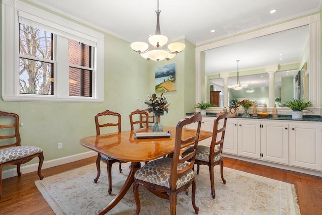 dining room with light wood-type flooring, a notable chandelier, crown molding, and baseboards