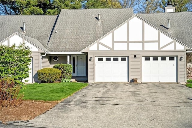 tudor house featuring a garage, a shingled roof, a front lawn, and aphalt driveway