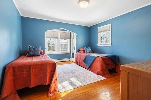 bedroom with multiple windows, wood-type flooring, and a baseboard heating unit