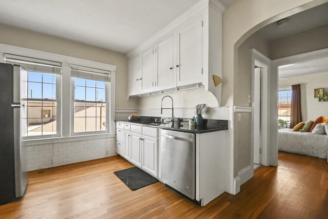 kitchen with light wood finished floors, stainless steel appliances, arched walkways, and a sink