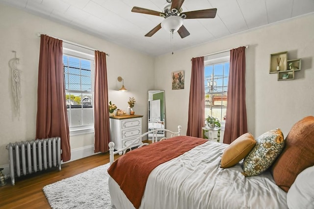 bedroom featuring radiator, baseboards, wood finished floors, and a ceiling fan