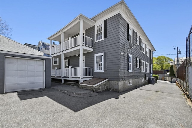 traditional home featuring aphalt driveway, an outdoor structure, a garage, and a balcony