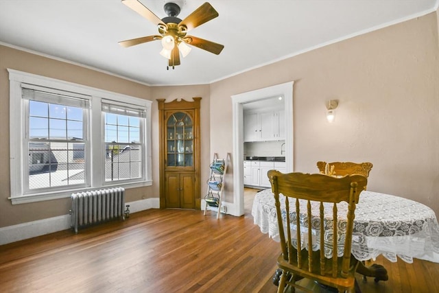 dining space featuring radiator, wood finished floors, ornamental molding, a ceiling fan, and baseboards