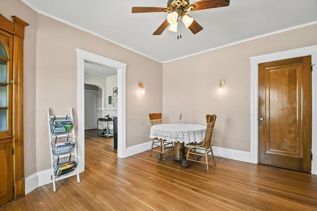 dining room featuring light wood finished floors, crown molding, arched walkways, a ceiling fan, and baseboards