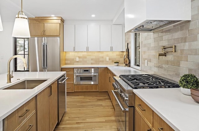 kitchen featuring pendant lighting, high quality appliances, sink, white cabinets, and custom exhaust hood