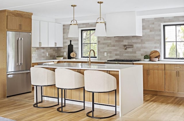 kitchen with white cabinetry, high quality fridge, pendant lighting, a kitchen island with sink, and backsplash