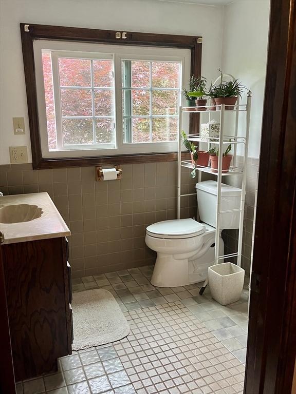 half bathroom with tile walls, toilet, tile patterned floors, vanity, and wainscoting