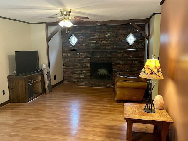 living room with a fireplace, ceiling fan, light wood finished floors, baseboards, and ornamental molding