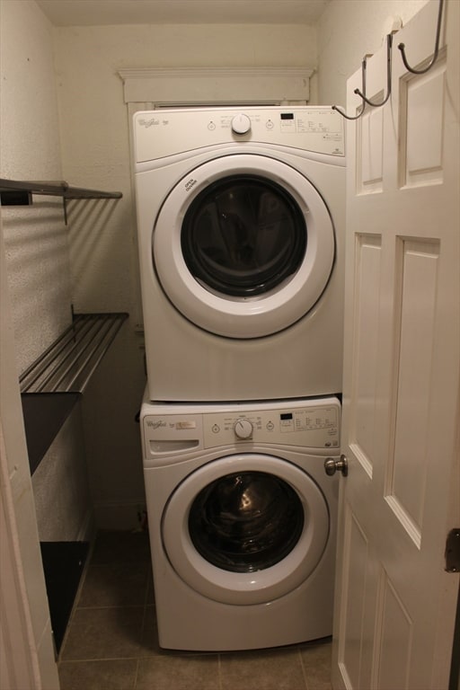 laundry area with stacked washing maching and dryer and dark tile patterned floors