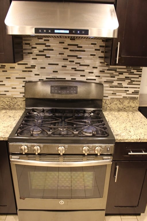 kitchen featuring decorative backsplash, gas stove, ventilation hood, and light stone countertops