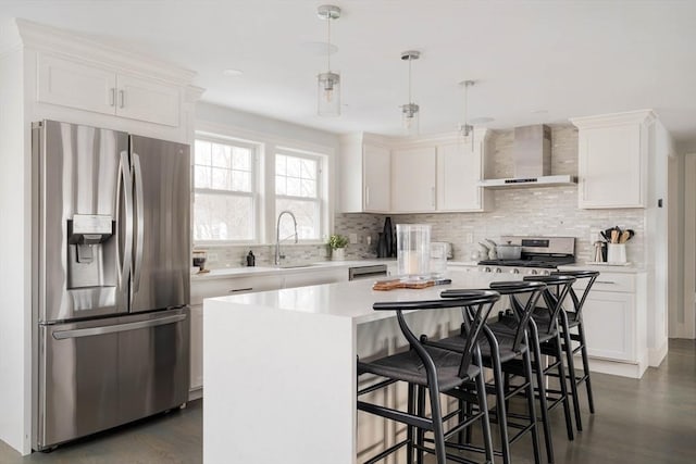 kitchen featuring wall chimney range hood, a center island, white cabinetry, hanging light fixtures, and appliances with stainless steel finishes