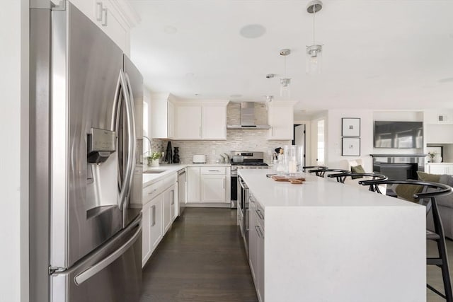 kitchen with white cabinetry, stainless steel appliances, decorative light fixtures, wall chimney range hood, and a center island