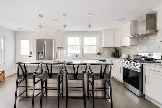 kitchen with stainless steel appliances, white cabinets, decorative light fixtures, and wall chimney range hood