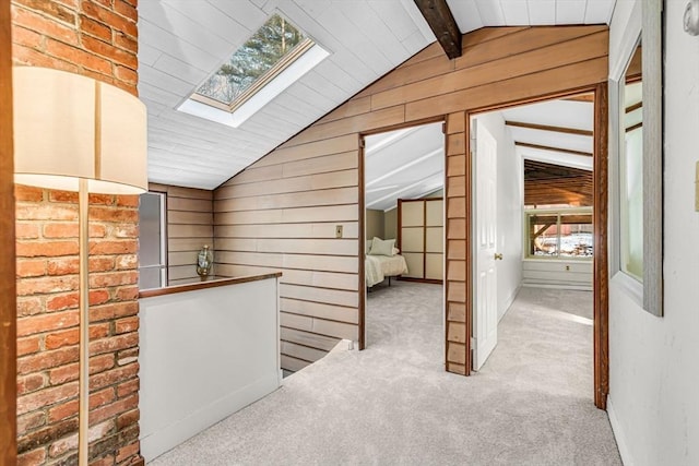 hall featuring vaulted ceiling with skylight, wood walls, carpet, and an upstairs landing