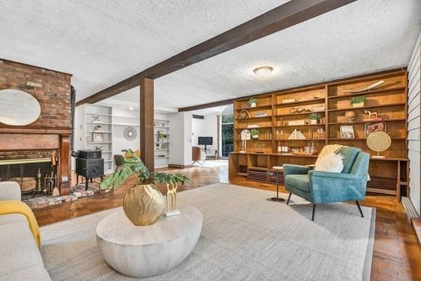 sitting room with a textured ceiling, built in shelves, beamed ceiling, and a brick fireplace