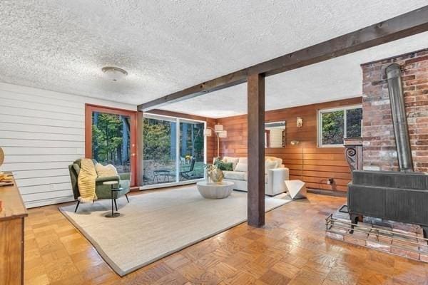 living area featuring a wood stove, wood walls, a textured ceiling, and beam ceiling