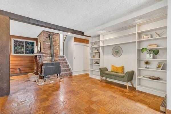 sitting room with a wood stove, a textured ceiling, and beam ceiling