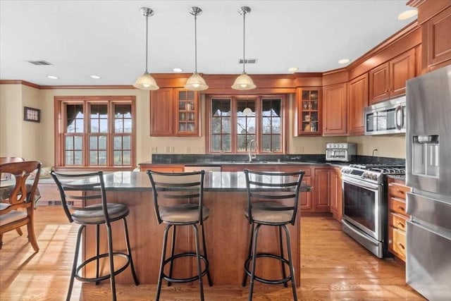 kitchen with appliances with stainless steel finishes, pendant lighting, a kitchen island, crown molding, and light hardwood / wood-style flooring