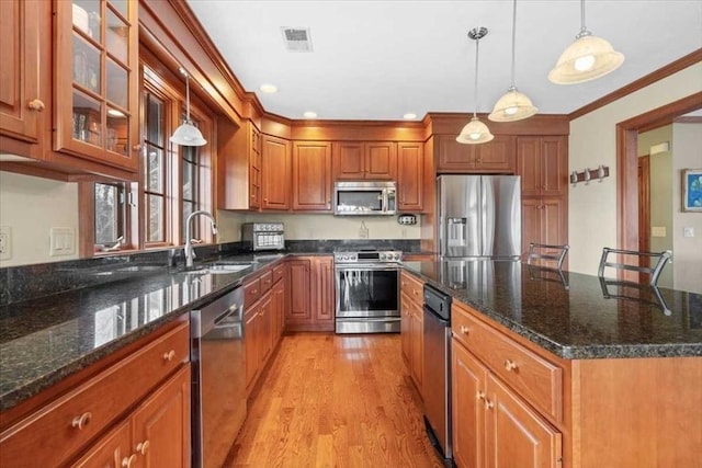 kitchen with dark stone countertops, light hardwood / wood-style floors, pendant lighting, sink, and stainless steel appliances