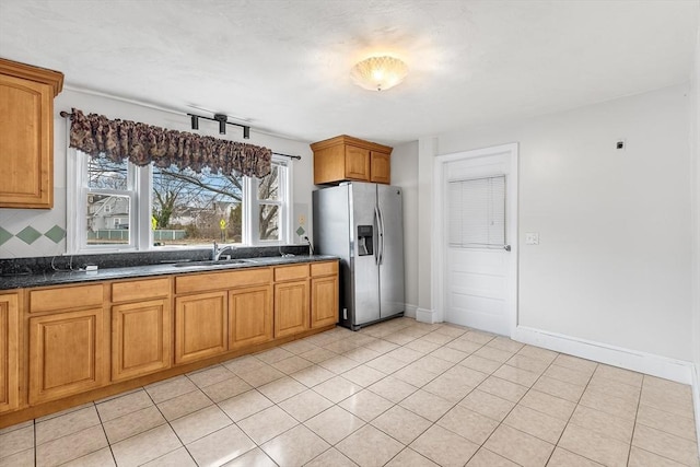 kitchen featuring stainless steel fridge, light tile patterned floors, dark stone counters, and sink