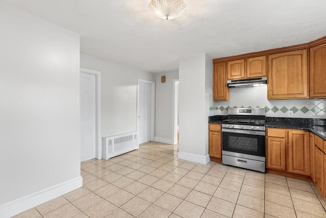 kitchen featuring radiator, decorative backsplash, dark stone countertops, light tile patterned flooring, and stainless steel range oven